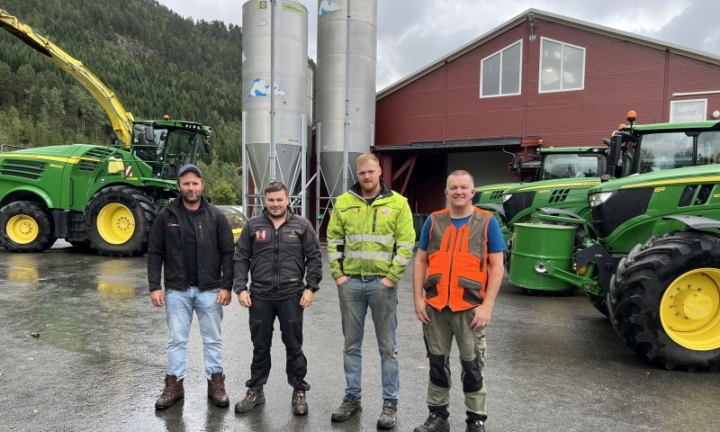 Fire bønder foran fjøs, traktorer og finsnitter.