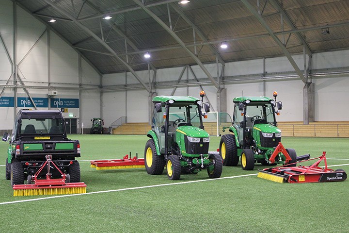 Gator og John Deere traktorer oppstilt ved midtsirkelen sammen med utstyr for vedlikehold av kunstgress