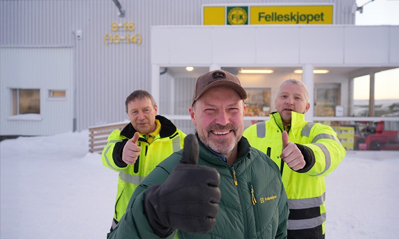 Tre karer med tommel opp foran bygning.