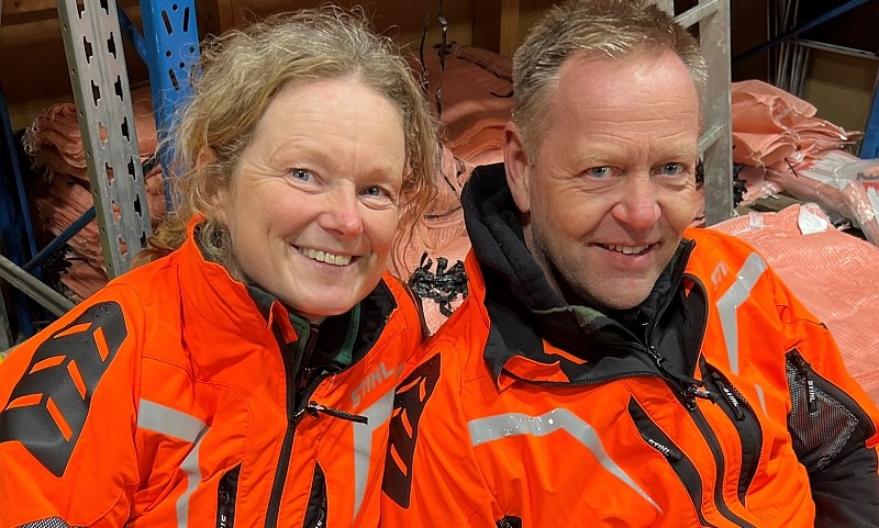 To personer i skogsjakke med vedsekker i abkgrunnen