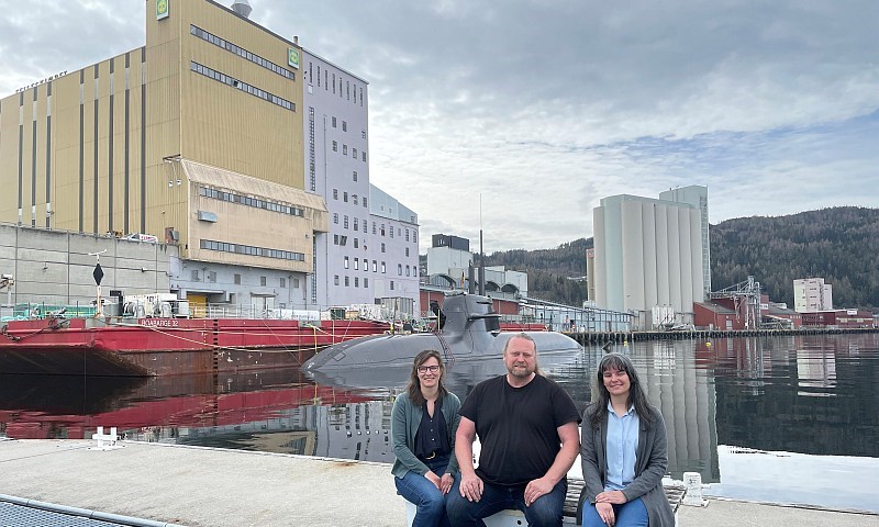 Gruppebilde foran kraftfôrfabrikk og brygge med ubåt