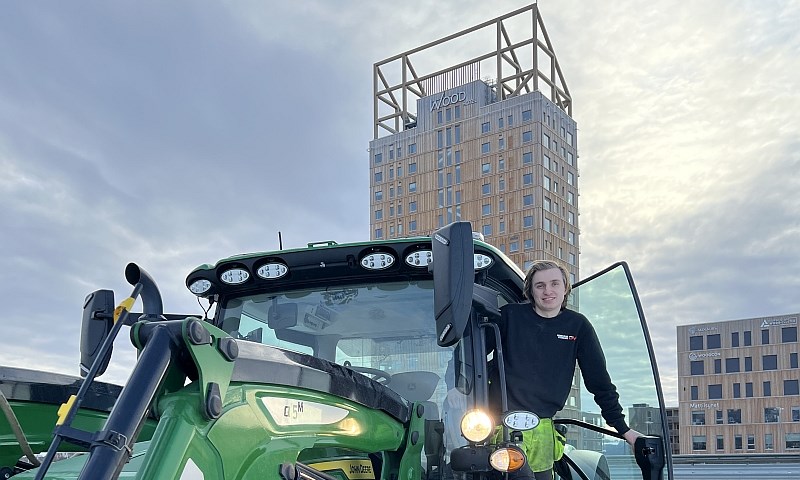 Ung mann i grønn traktor foran verdens høyeste trehus