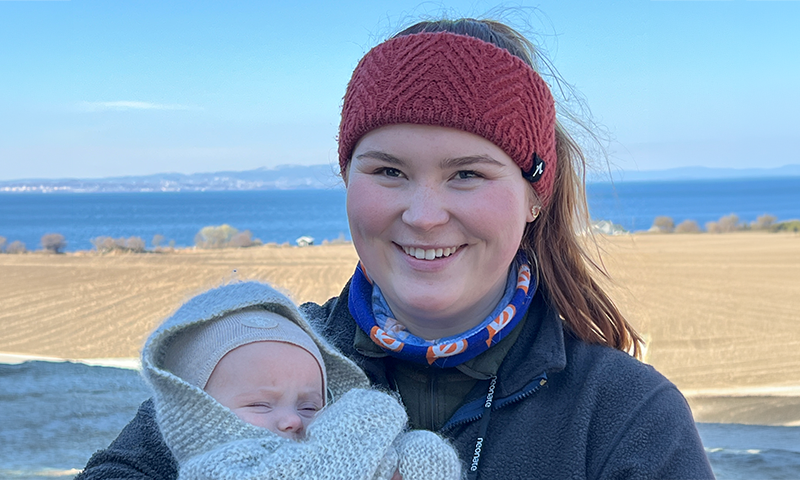 Ung bonde med barn på armen og Trondheimsfjorden bak