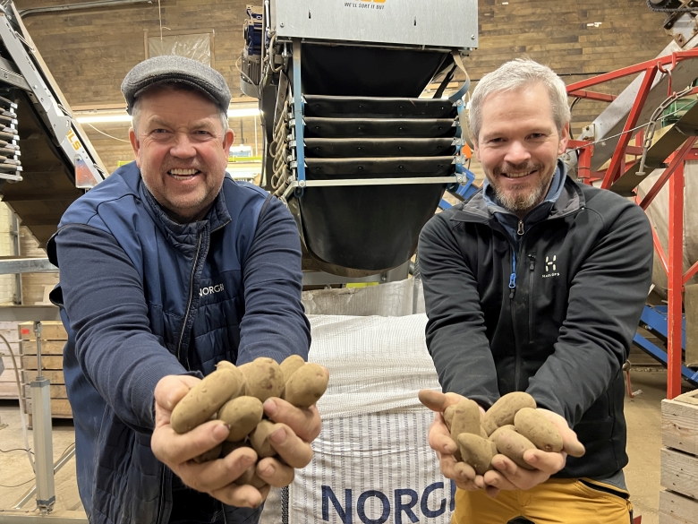 To menn med potet i hendene foran et sorteringsanlegg