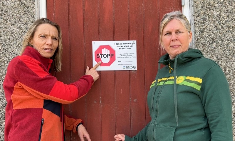 To damer utenfor fjøsdøra som har et stoppskilt.