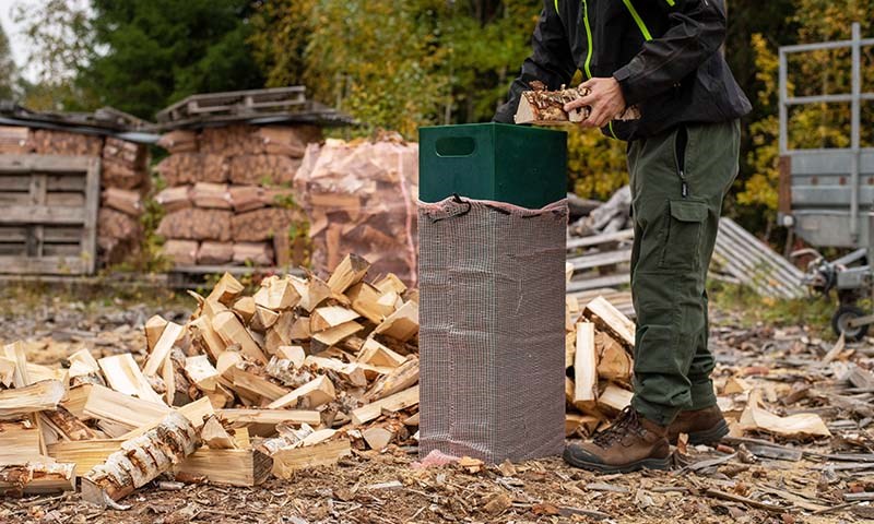 Mann som pakker ved i liten vedsekk ved hjelp av en sekkekanal